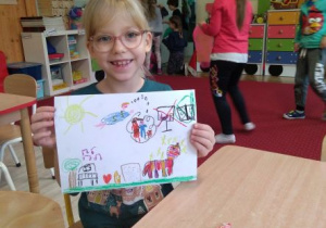 Dziewczynka trzyma przed sobą rysunek przedstawiający Świat Wyobraźni